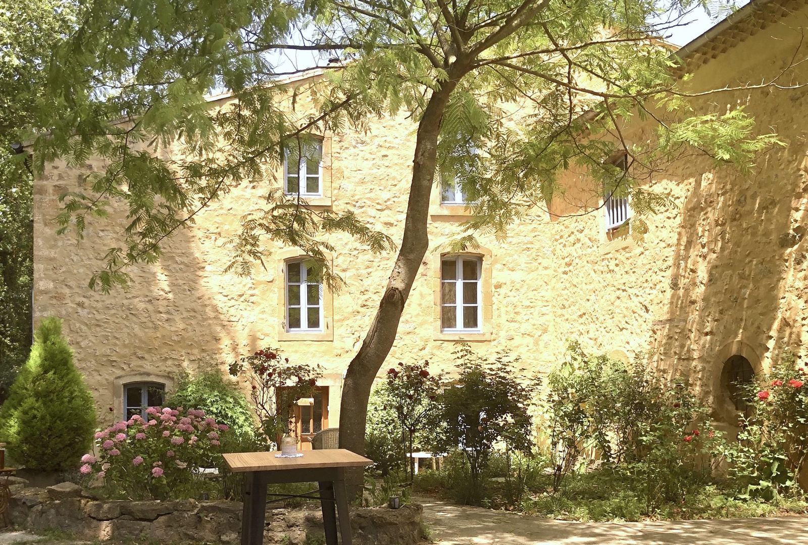 La façade en pierre dorée de la Bâtisse, rosiers et hortensias
