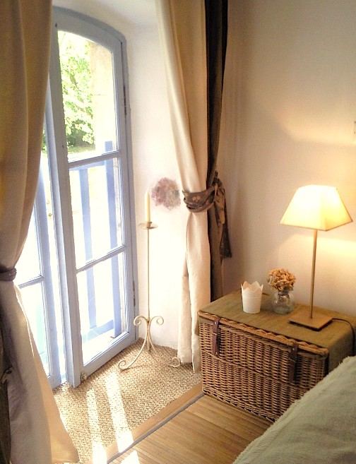 La chambre Garrigue : porte-fenêtre ouverte sur la verdure, malle en osier et lampe de chevet