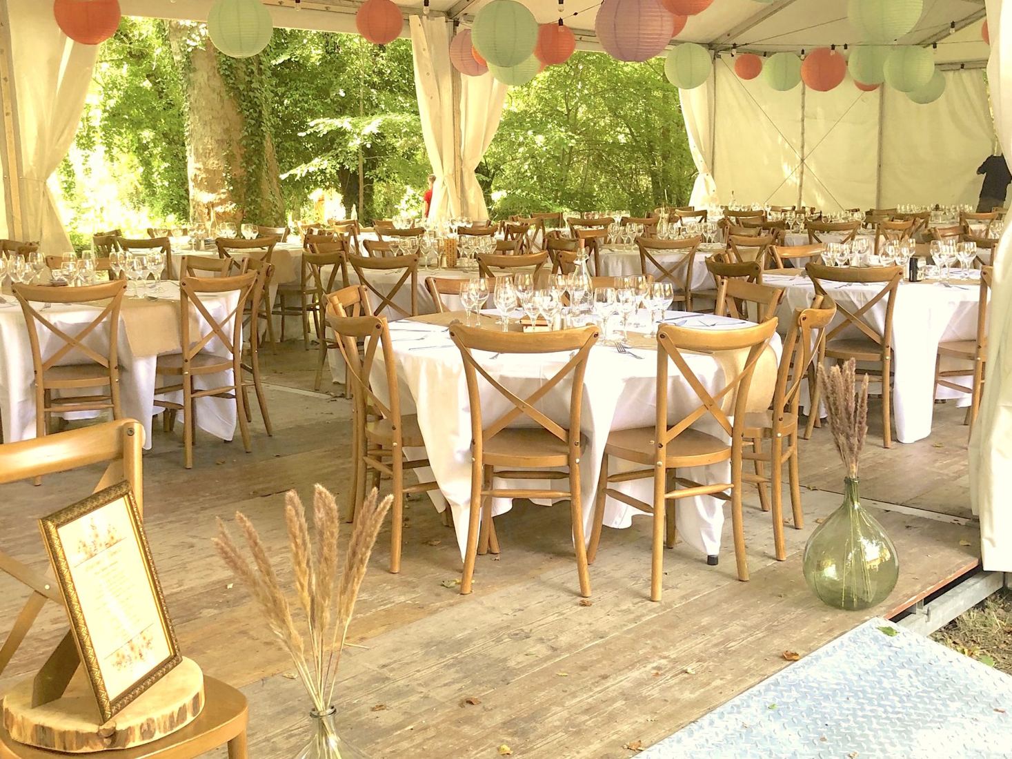 Tables dressées sous le chapiteau, lampions pastel et chaises en bois